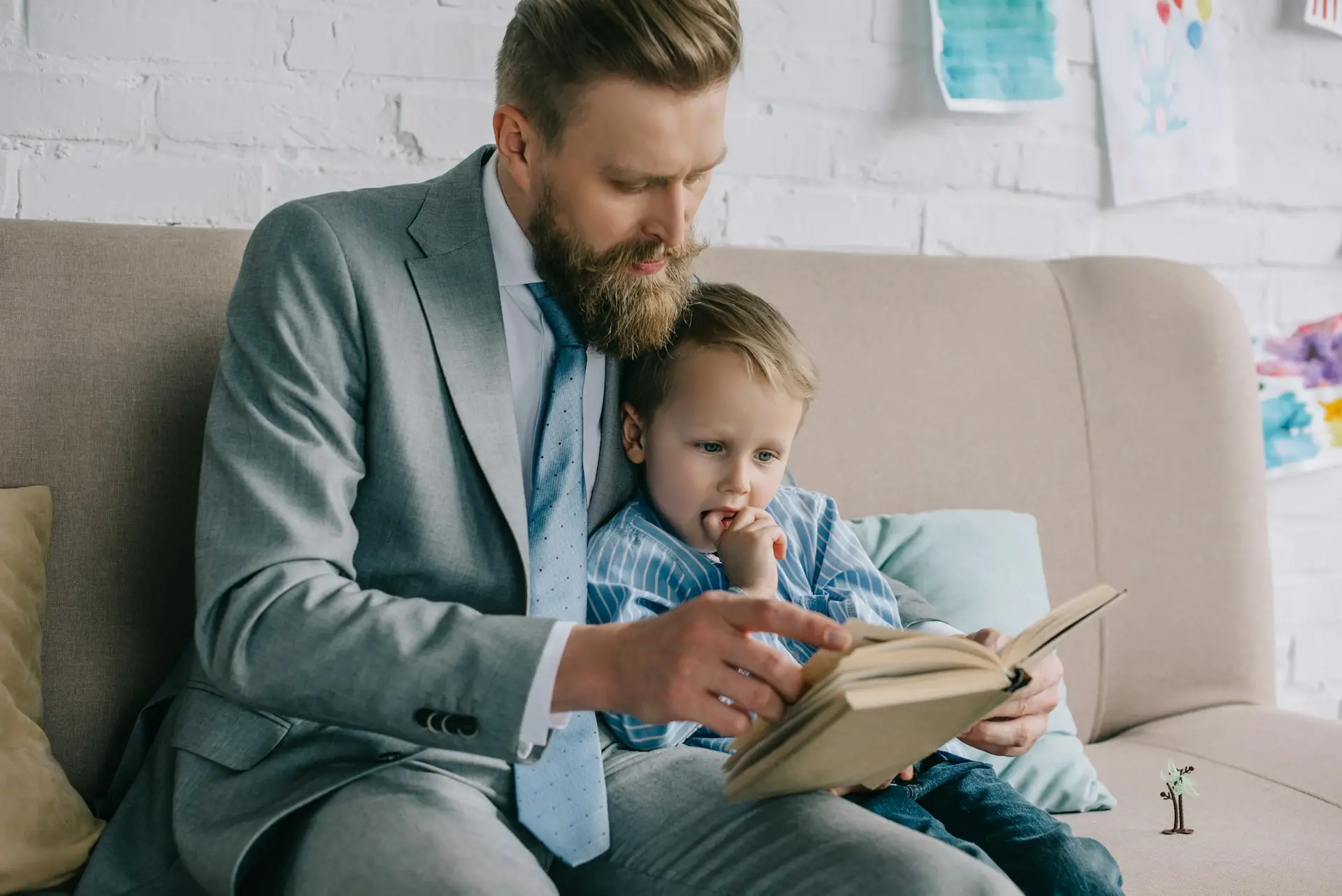 businessman and little son reading book together an sofa at home, work and life balance